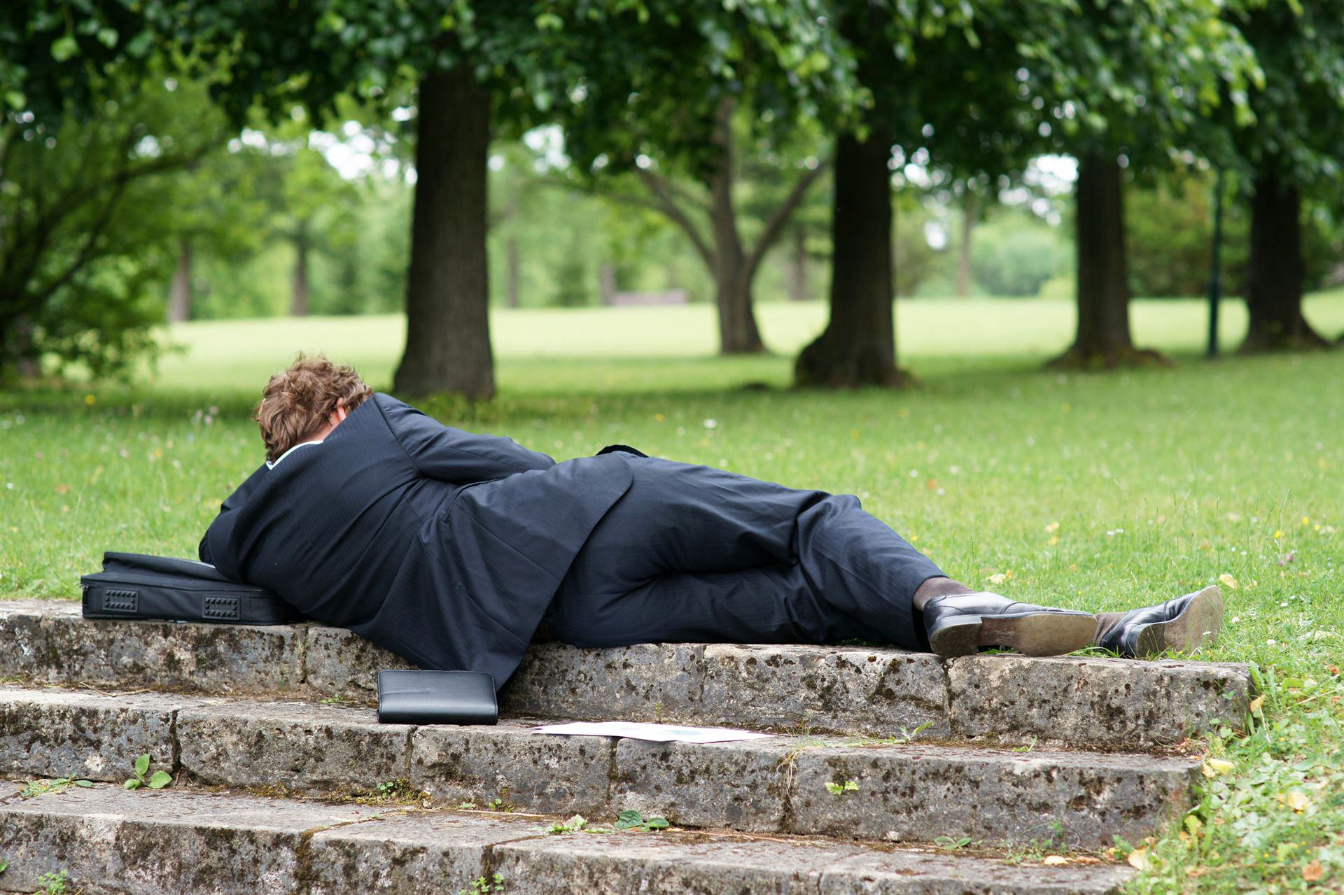 Ein Mann liegt auf dem Rasen und begeht Arbeitszeitbetrug, obwohl er arbeiten müsste.