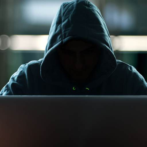 Vermummte Person mit Kaputzenpullover sitzt an einem Laptop