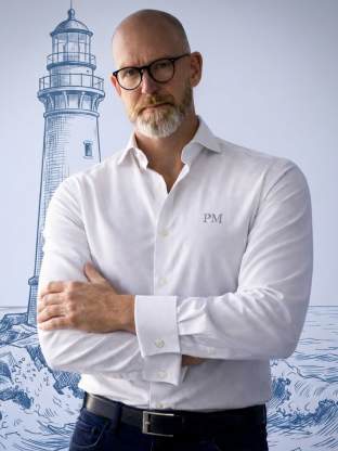 Paul H. Malberg vor der Kamera. Im Hintergrund ein Leuchtturm